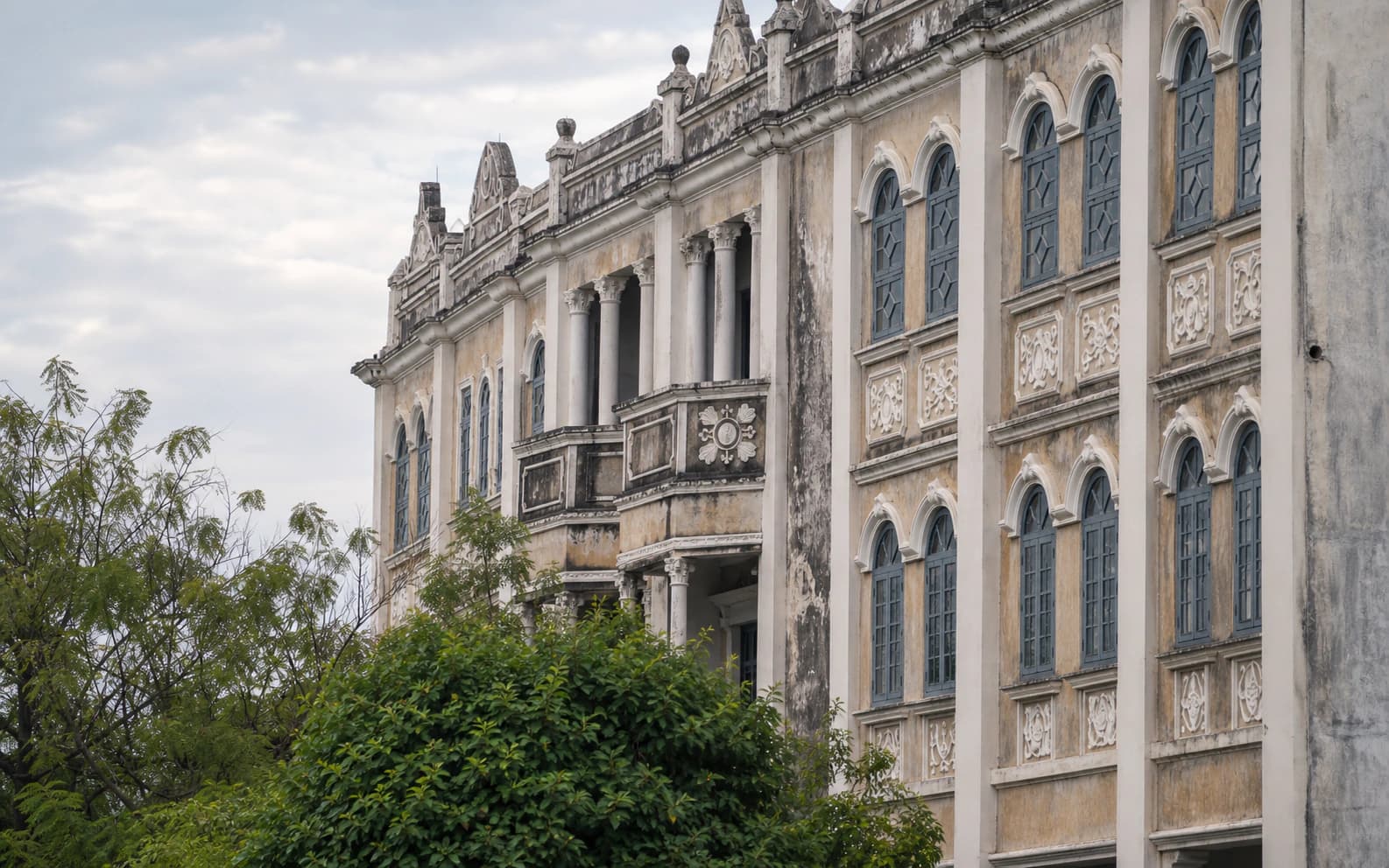 Weathered qilou facade with arched windows, columns and leafy foreground