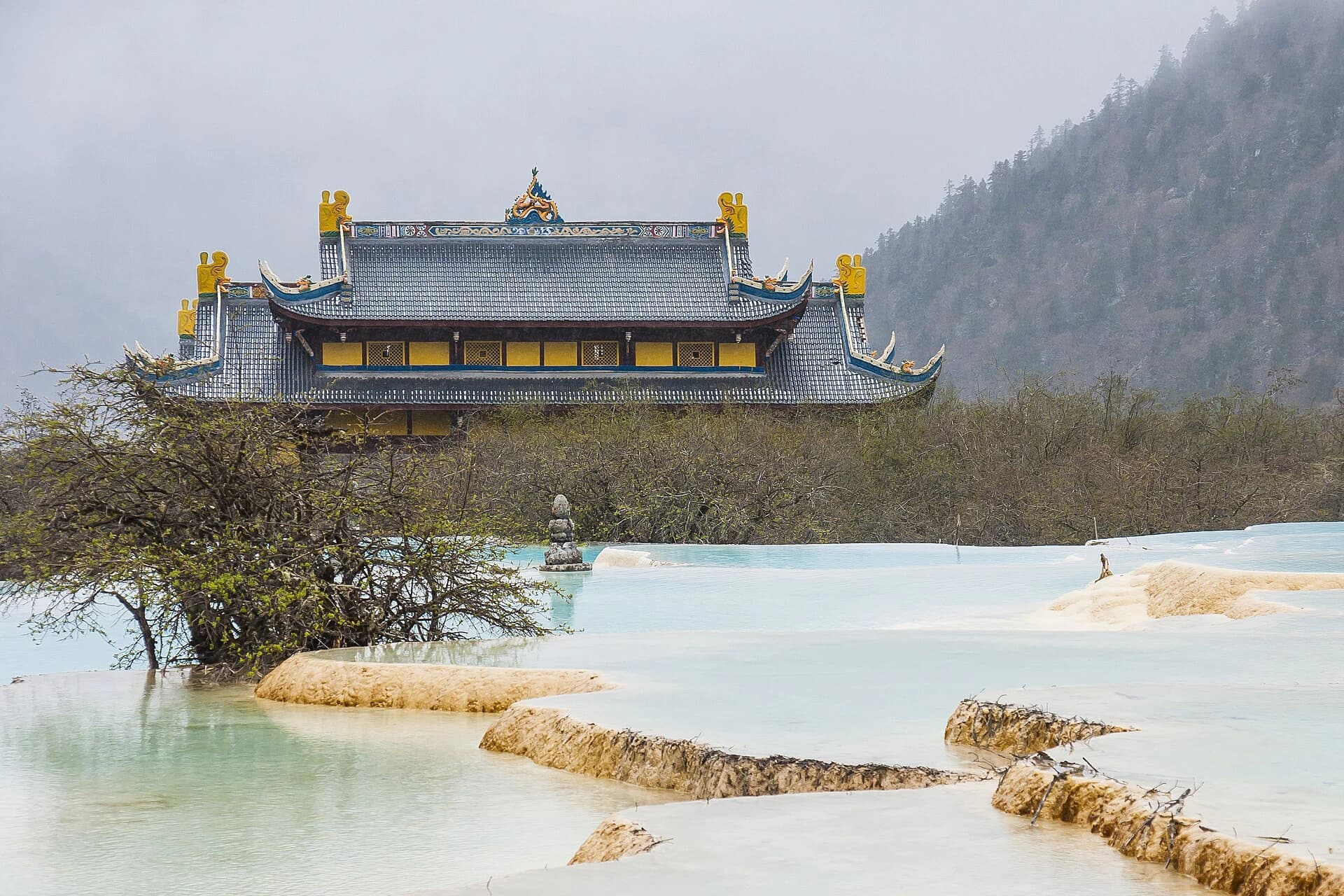 Tejado de un templo tras estanques pálidos de travertino en Huanglong