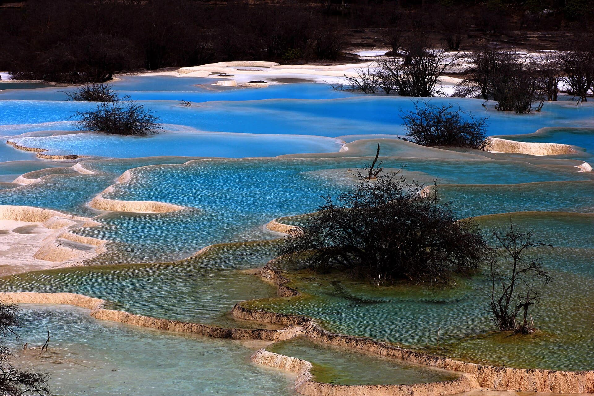 Agua transparente contenida en terrazas claras de travertino durante el descenso de Huanglong