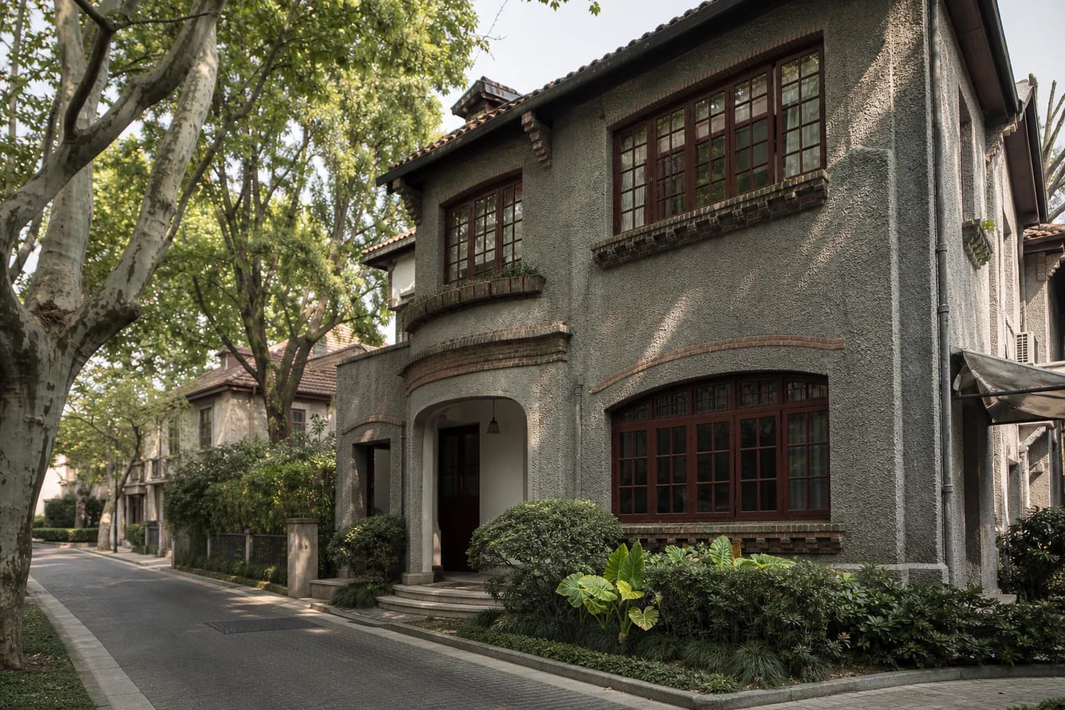 Una casa de jardín gris con ventanas de color rojo oscuro debajo de plátanos maduros