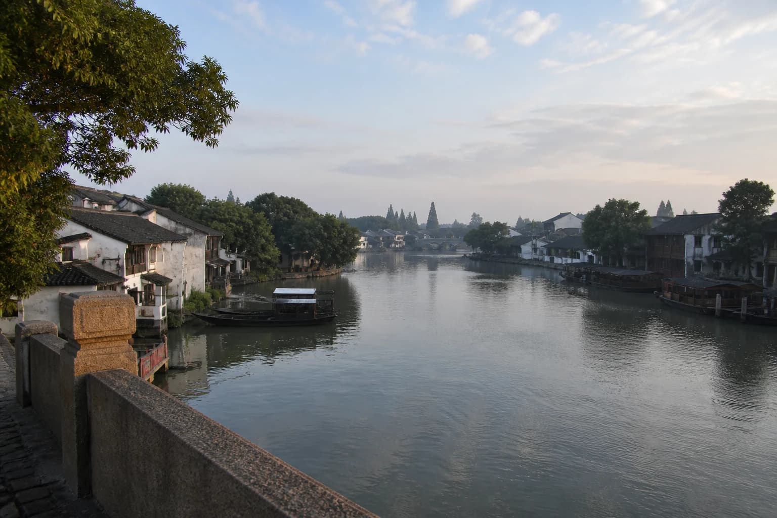 Una amplia vista del canal a primera hora de la mañana con barcos y casas bajas junto al agua en Zhujiajiao