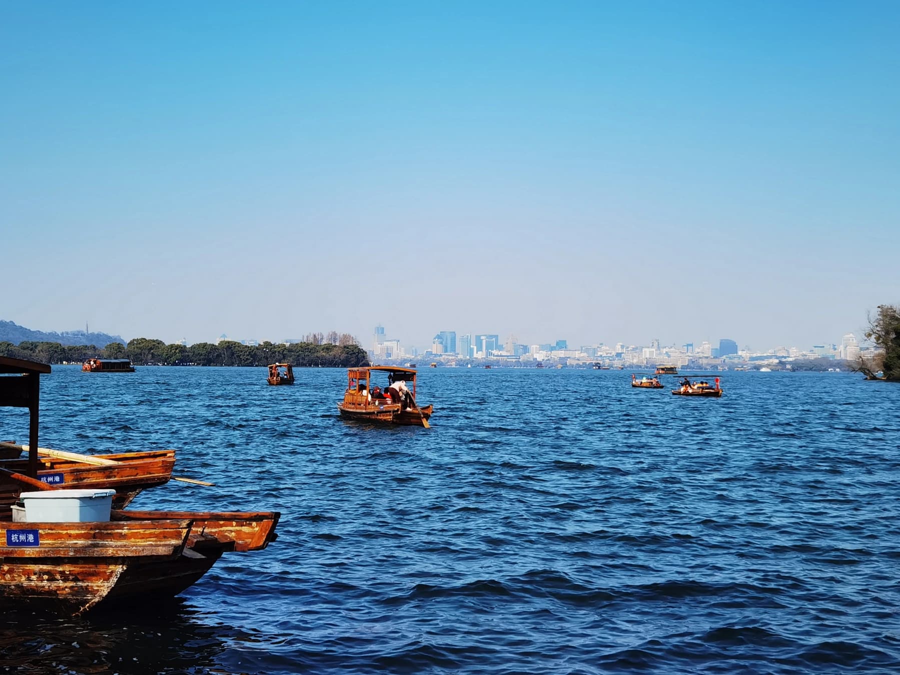 Barcos de pasajeros en West Lake, con aguas abiertas y edificios urbanos a lo lejos