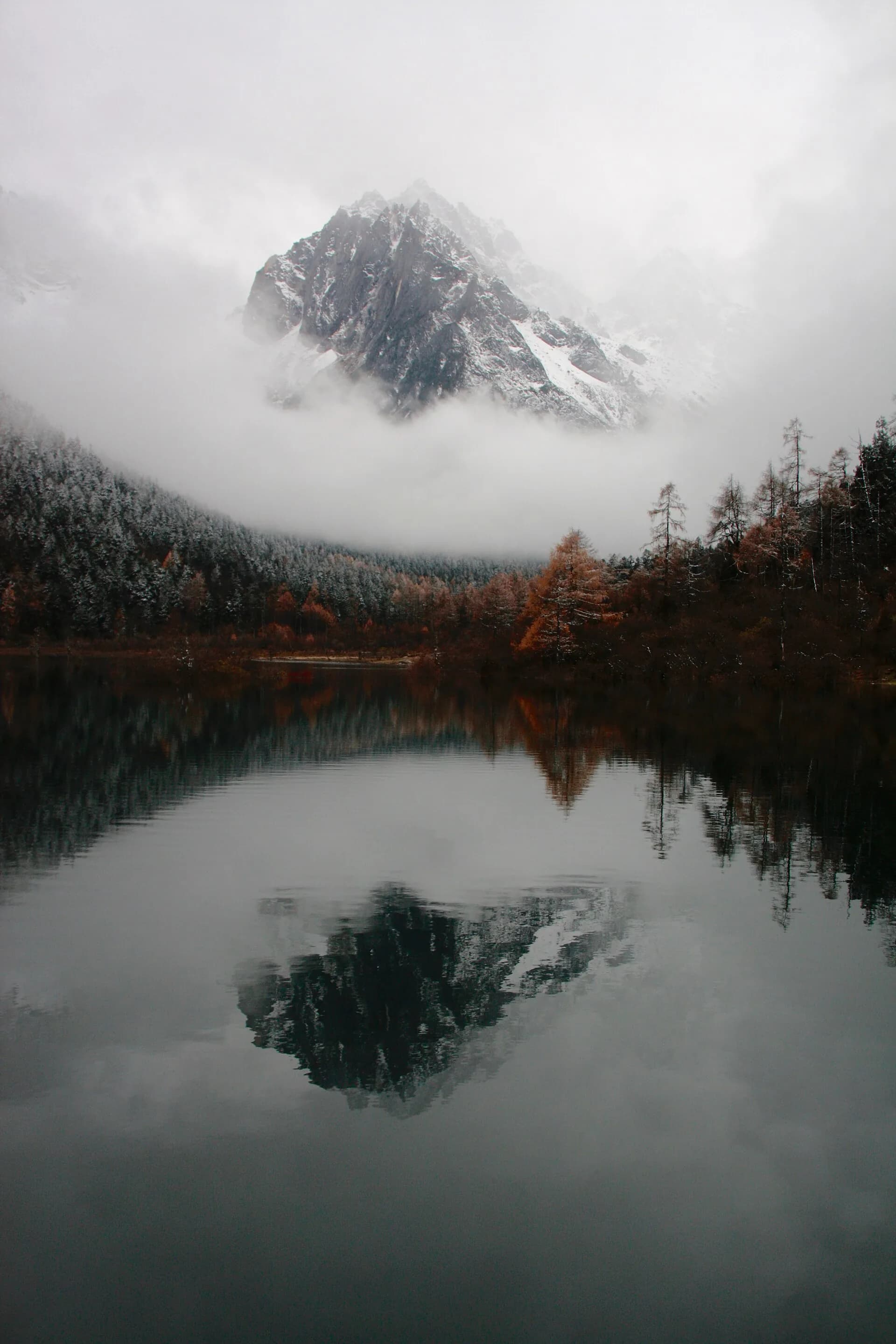 Mountain and forest reflected in a misty alpine lake in Bipenggou