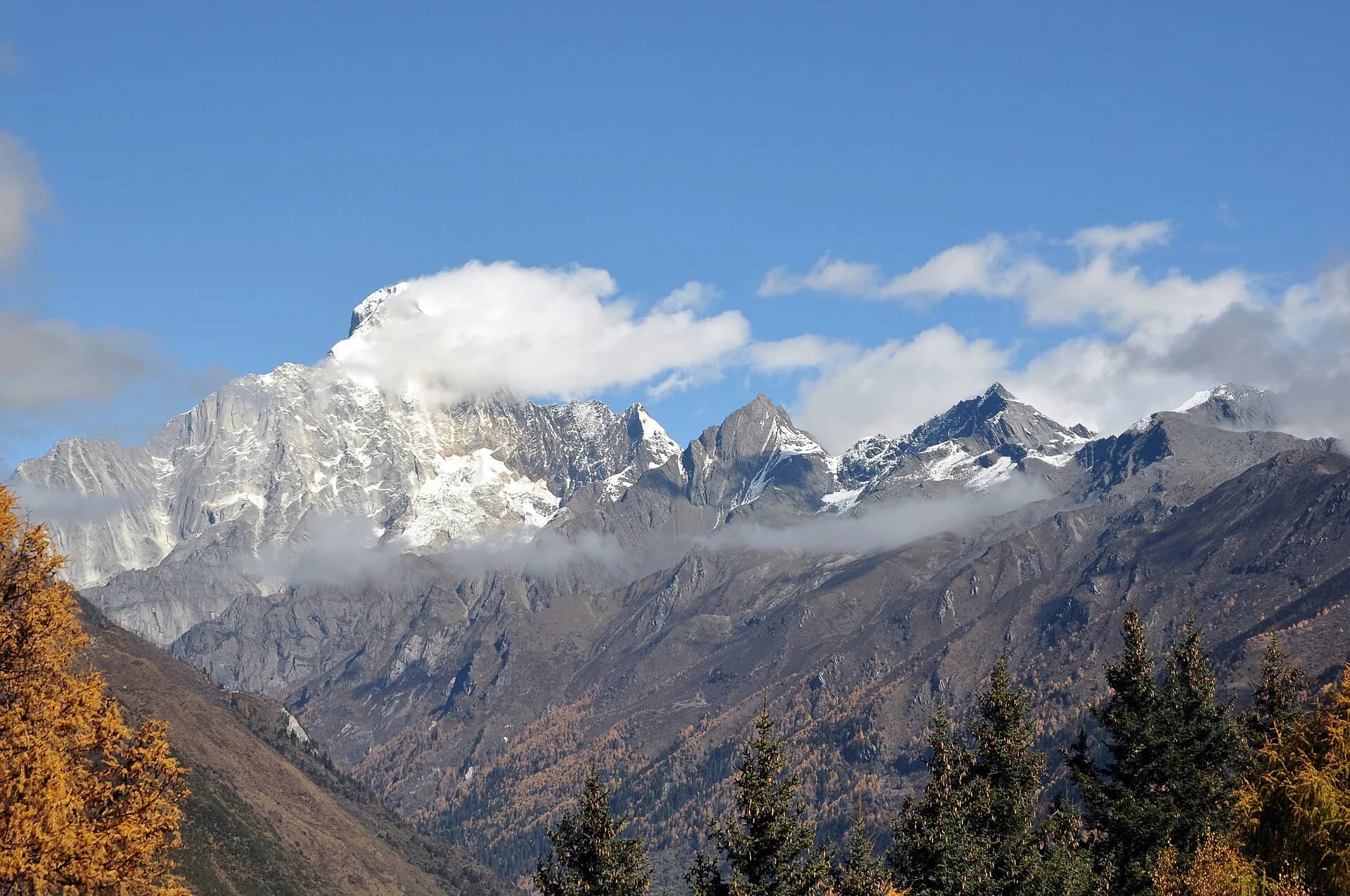 Four snow-covered peaks of the wider Mount Siguniang massif above high-country terrain