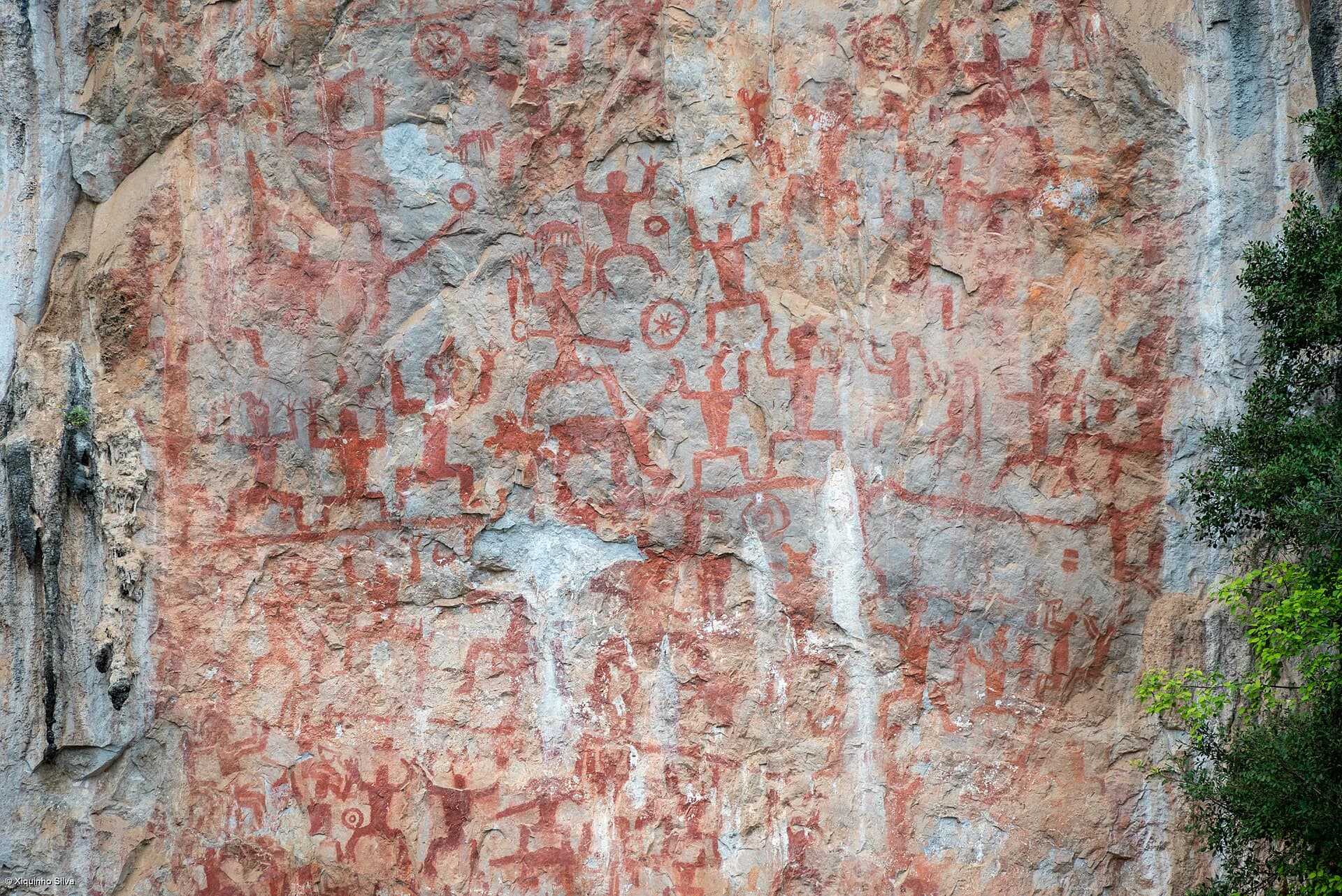 Dense group of red Huashan rock-art motifs on pale limestone