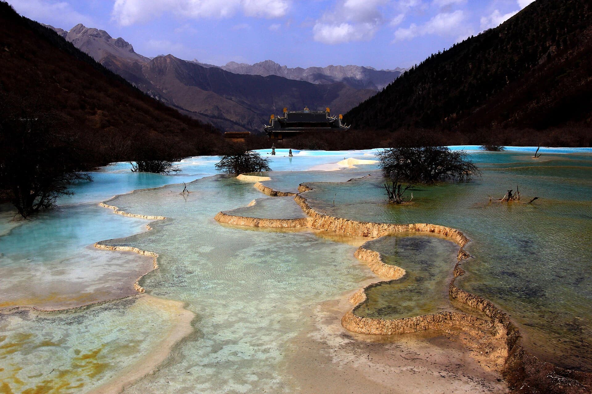 Blue-green Huanglong travertine pools below a temple and mountain ridge