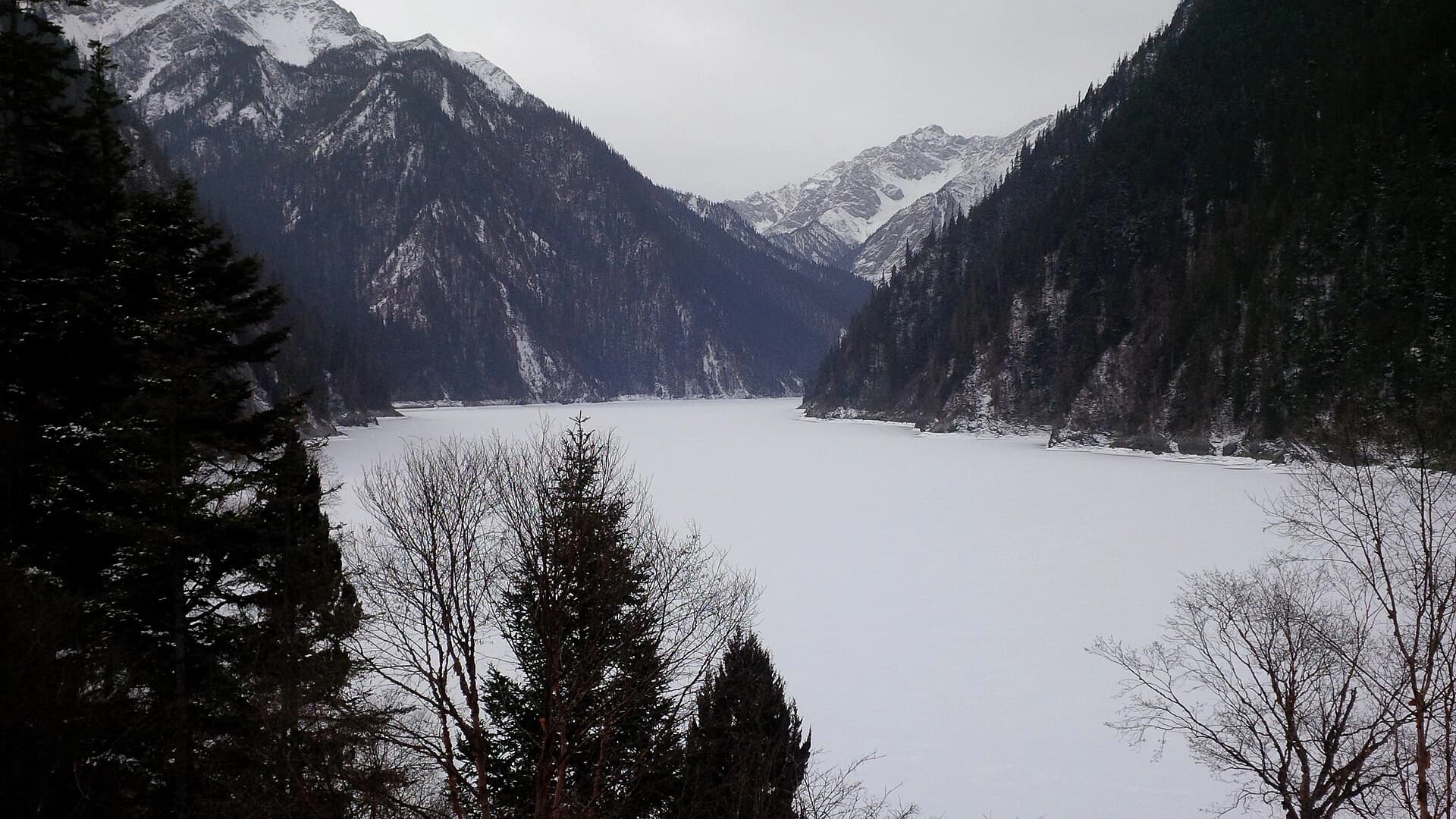 Frozen Long Lake surrounded by dark forest and snow-covered mountains in winter