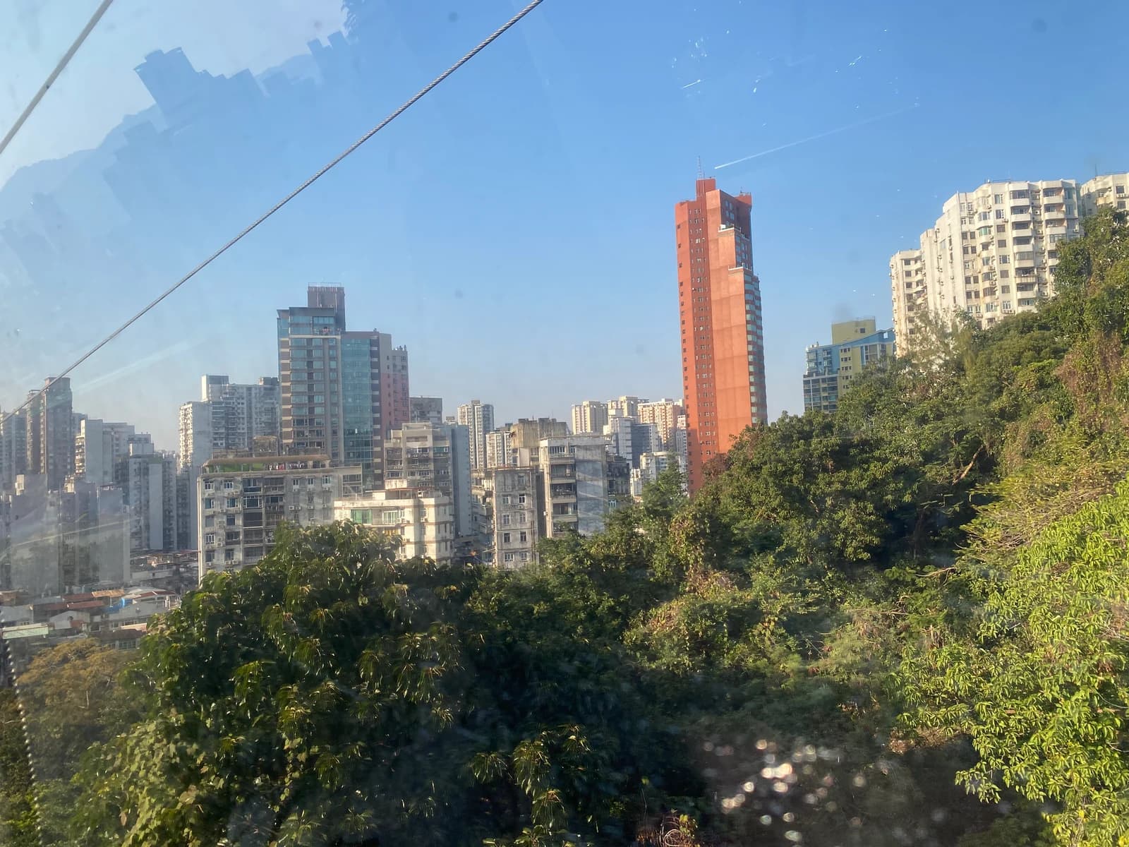 Horizonte residencial de Macao y ladera verde vistos desde la ventana del teleférico de la colina de Guia