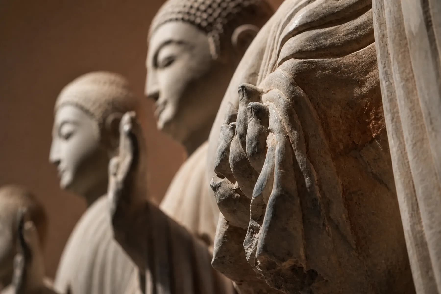 Primer plano de una mano y los pliegues de la túnica de una escultura budista en piedra desgastada