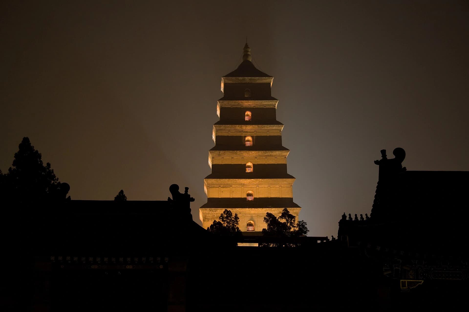 Vista documental nocturna de la Gran Pagoda del Ganso Salvaje iluminada sobre las siluetas de los tejados del templo