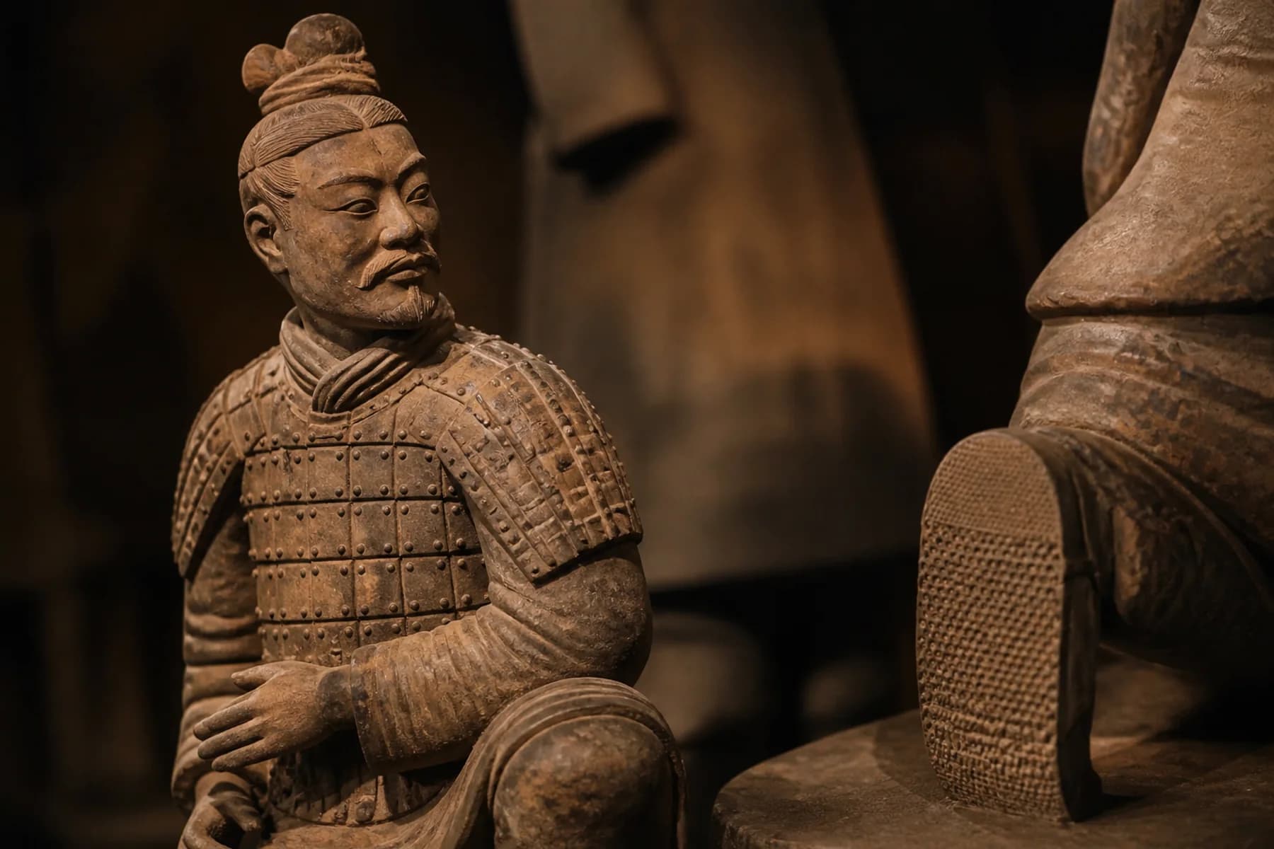 Vista de cerca editorial que destaca la armadura de terracota, las manos modeladas, el cabello y una suela de zapato con patrón