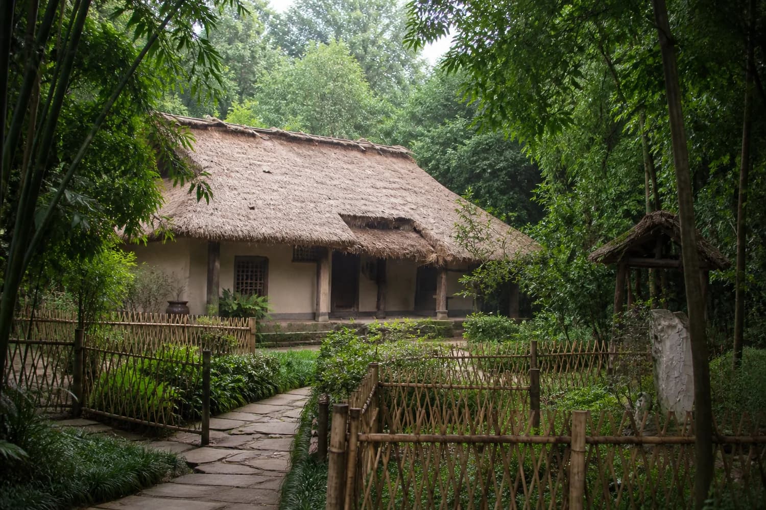 Cabaña de techo de paja reconstruida con cercado de bambú en el jardín del museo