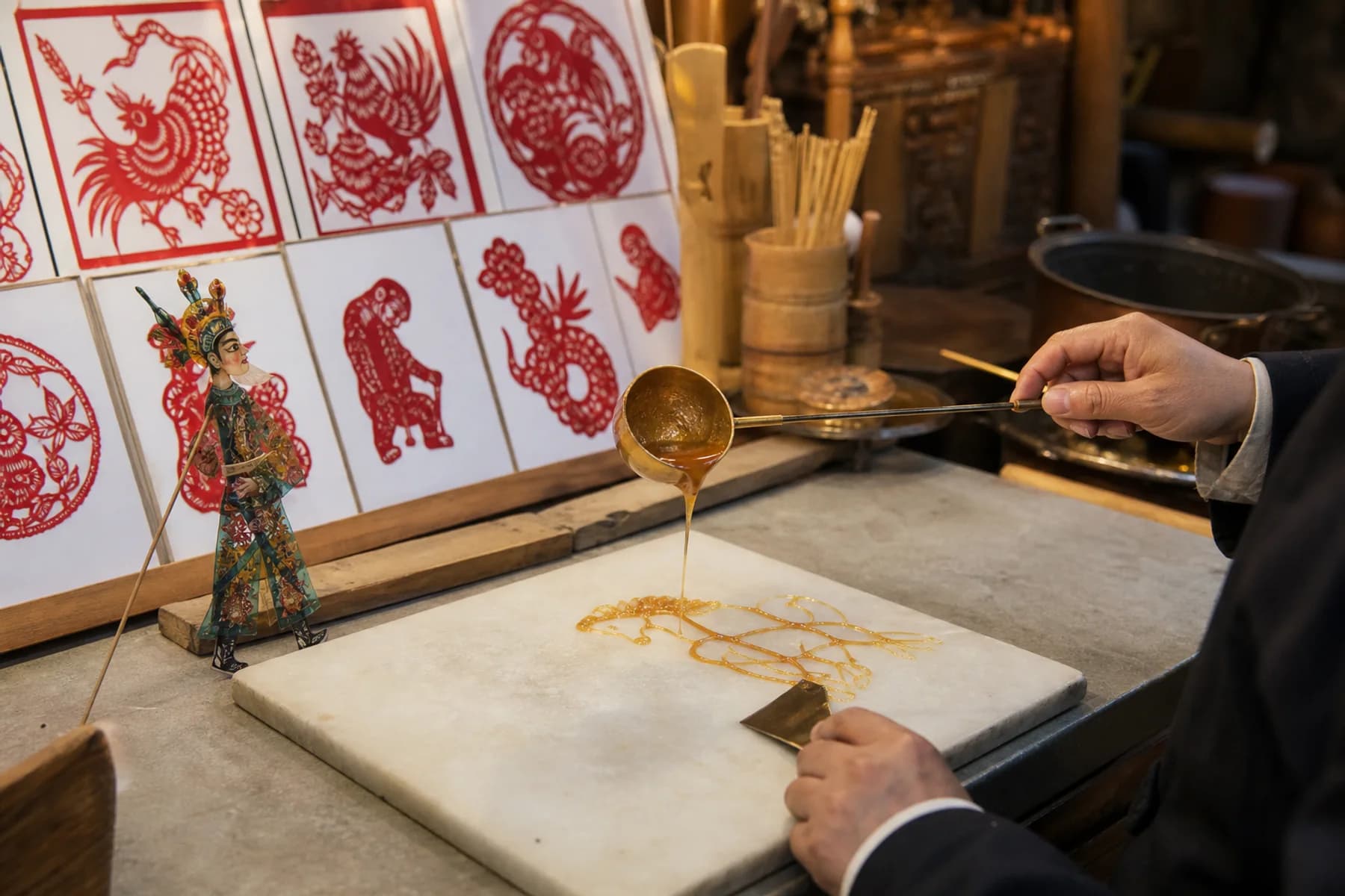 Escena de pintura con azúcar junto a recorte de papel y una figura de sombras chinescas de Sichuan